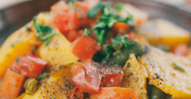 Tajine de poulet aux épices avec légumes et olives, servi dans un plat en terre cuite.