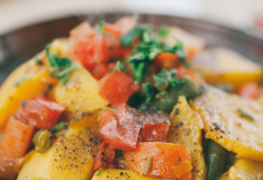 Tajine de poulet aux épices avec légumes et olives, servi dans un plat en terre cuite.