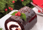 Bûche de Noël au chocolat, décorée de copeaux de chocolat et de sucre glace, sur une table festive.