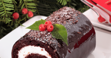 Bûche de Noël au chocolat, décorée de copeaux de chocolat et de sucre glace, sur une table festive.