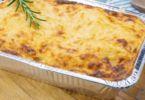 Lasagnes dorées à la bolognaise, servies dans un plat individuel avec des herbes fraîches en garniture.