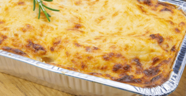 Lasagnes dorées à la bolognaise, servies dans un plat individuel avec des herbes fraîches en garniture.