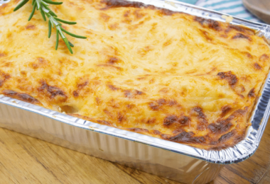 Lasagnes dorées à la bolognaise, servies dans un plat individuel avec des herbes fraîches en garniture.