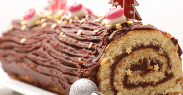 Bûche de Noël aux agrumes et amandes caramélisées, joliment présentée avec des zestes et des décorations festives.