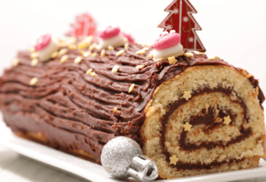 Bûche de Noël aux agrumes et amandes caramélisées, joliment présentée avec des zestes et des décorations festives.