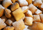 Beignets feuilletés dorés et saupoudrés de sucre, prêts à être dégustés.