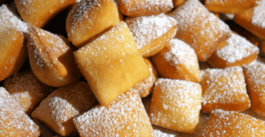 Beignets feuilletés dorés et saupoudrés de sucre, prêts à être dégustés.