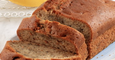 Banana bread moelleux et doré, servi avec des tranches de banane et des noix en garniture.