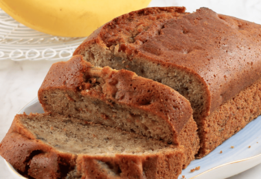 Banana bread moelleux et doré, servi avec des tranches de banane et des noix en garniture.