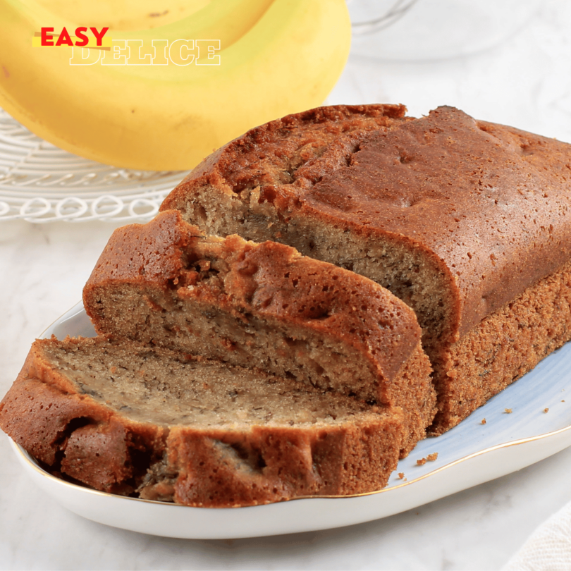 Banana bread moelleux et doré, servi avec des tranches de banane et des noix en garniture.