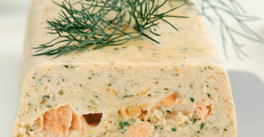 Terrine de saumon moelleuse et colorée, servie avec des tranches de citron et de l’aneth frais.