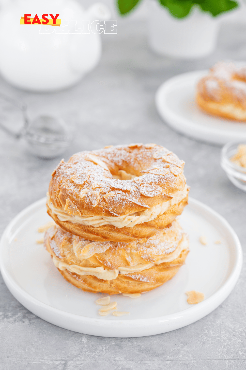 Un Paris-Brest doré, garni d’une crème mousseline pralinée, saupoudré de sucre glace et décoré de noisettes.