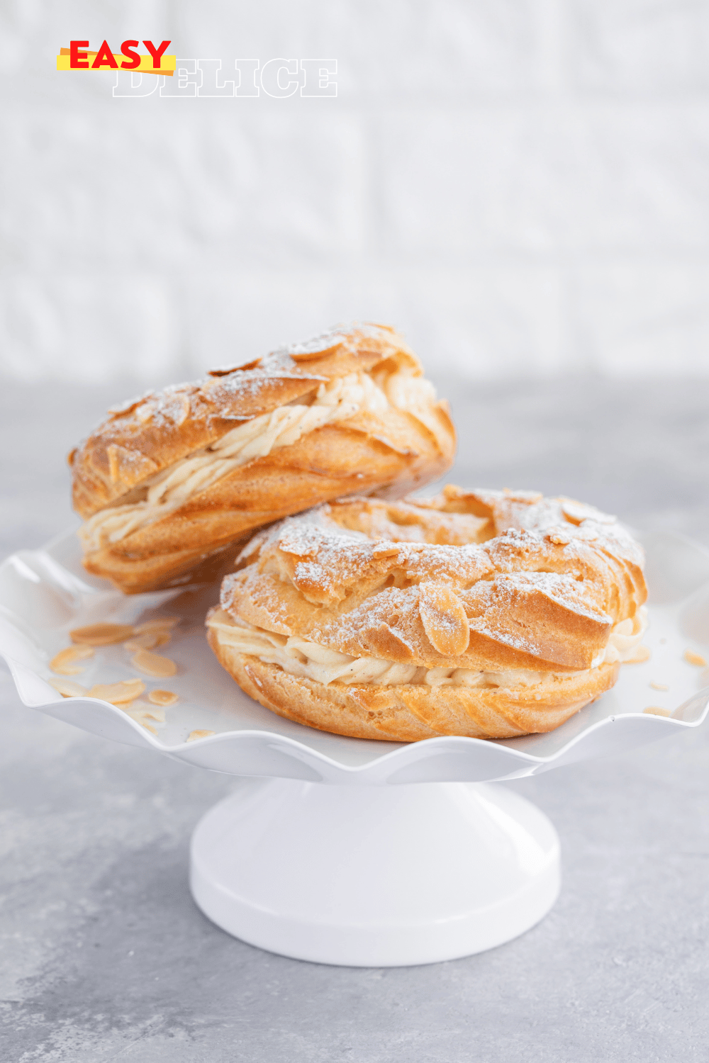 Un Paris-Brest doré, garni d’une crème mousseline pralinée, saupoudré de sucre glace et décoré de noisettes.