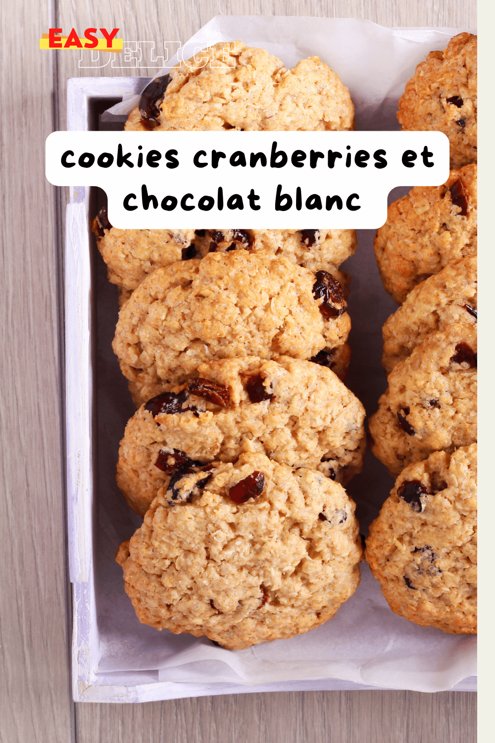 Cookies cranberries et chocolat blanc dorés, disposés sur une grille de refroidissement avec des morceaux de chocolat blanc et des cranberries en arrière-plan.