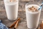 Horchata au lait servie dans un verre, décorée avec une pincée de cannelle et une tige de cannelle en garniture.