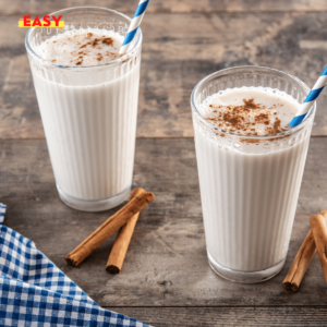 Horchata au lait servie dans un verre, décorée avec une pincée de cannelle et une tige de cannelle en garniture.