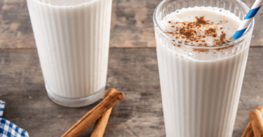 Horchata au lait servie dans un verre, décorée avec une pincée de cannelle et une tige de cannelle en garniture.