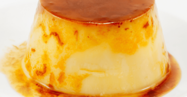 Flan coco doré et fondant, servi dans une assiette avec une garniture de noix de coco râpée.