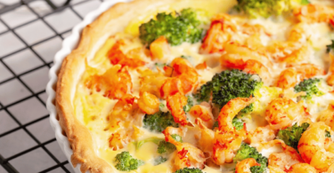 Une quiche dorée et appétissante aux crevettes et brocoli, tranchée et servie avec une salade verte.