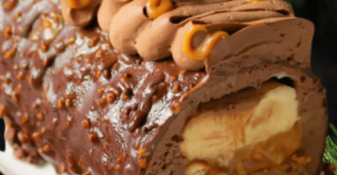 Une bûche chocolat, cacahuète et caramel décorée avec des cacahuètes caramélisées et des éclats de chocolat.