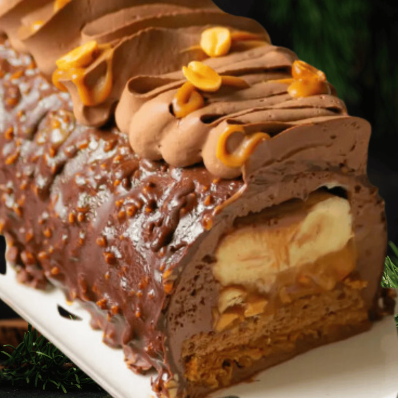 Une bûche chocolat, cacahuète et caramel décorée avec des cacahuètes caramélisées et des éclats de chocolat.