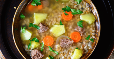 Bol de Krupnik polonais avec orge, légumes et viande, servi chaud avec du persil frais.