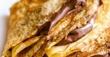 Une pile de crêpes dorées et moelleuses, garnies de sucre glace et de fruits frais.