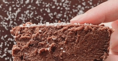 Gâteau fondant au chocolat servi avec une cuillère de compote et une décoration de copeaux de chocolat.