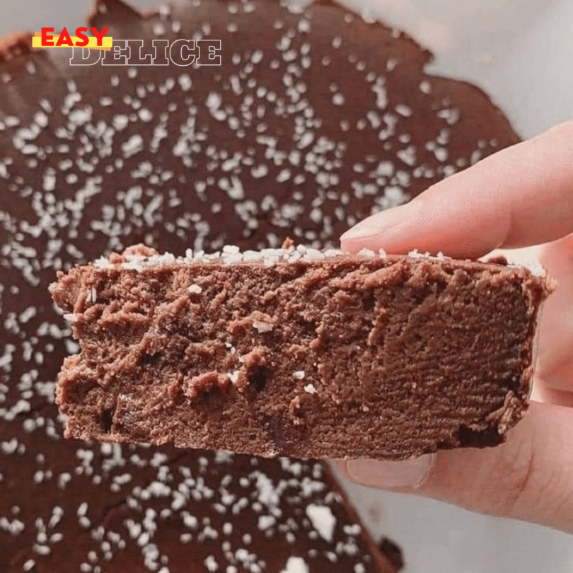 Gâteau fondant au chocolat servi avec une cuillère de compote et une décoration de copeaux de chocolat.