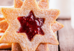 Sablés Linzer garnis de confiture de framboise, saupoudrés de sucre glace sur une assiette festive.