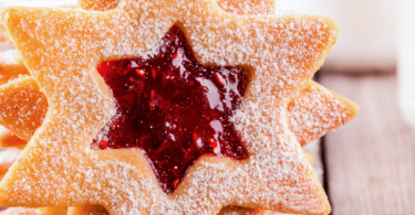 Sablés Linzer garnis de confiture de framboise, saupoudrés de sucre glace sur une assiette festive.