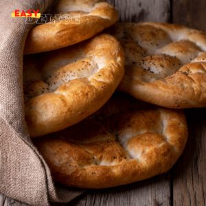 Pain pide doré, saupoudré de graines de sésame et de nigelle, servi sur une table festive.