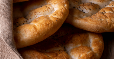 Pain pide doré, saupoudré de graines de sésame et de nigelle, servi sur une table festive.