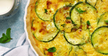 Quiche aux courgettes dorée, garnie de rondelles de courgette et d’œufs, servie avec une salade verte.