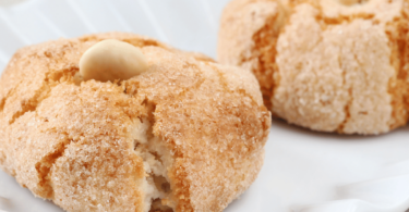 Biscuits amaretti moelleux, saupoudrés de sucre glace, servis sur une assiette.