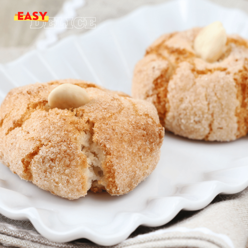 Biscuits amaretti moelleux, saupoudrés de sucre glace, servis sur une assiette.