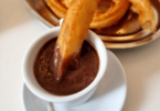 Une assiette de churros dorés saupoudrés de sucre, accompagnés d’un bol de chocolat chaud.