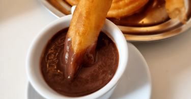 Une assiette de churros dorés saupoudrés de sucre, accompagnés d’un bol de chocolat chaud.