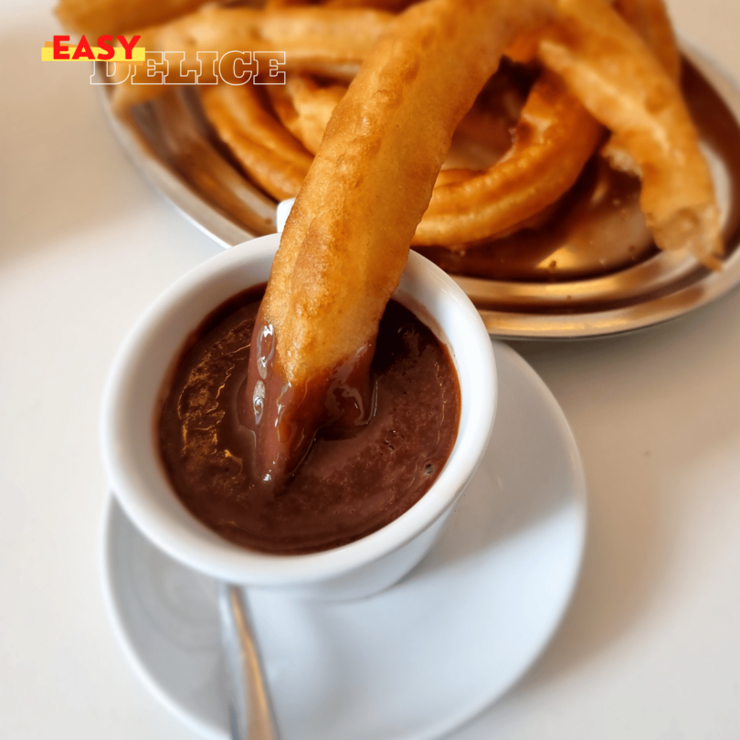 Une assiette de churros dorés saupoudrés de sucre, accompagnés d’un bol de chocolat chaud.