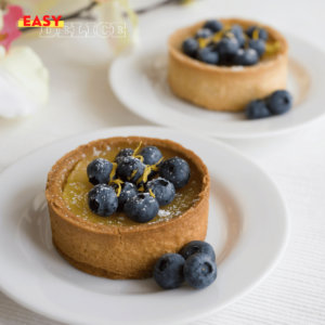 Tarte citron myrtilles garnie de fruits frais, présentée sur un plateau élégant.