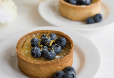 Tarte citron myrtilles garnie de fruits frais, présentée sur un plateau élégant.