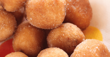 Beignets de carnaval dorés et saupoudrés de sucre glace, présentés dans une assiette festive.