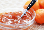 Pot de confiture de mandarines maison avec des tranches de mandarines fraîches et zestes.