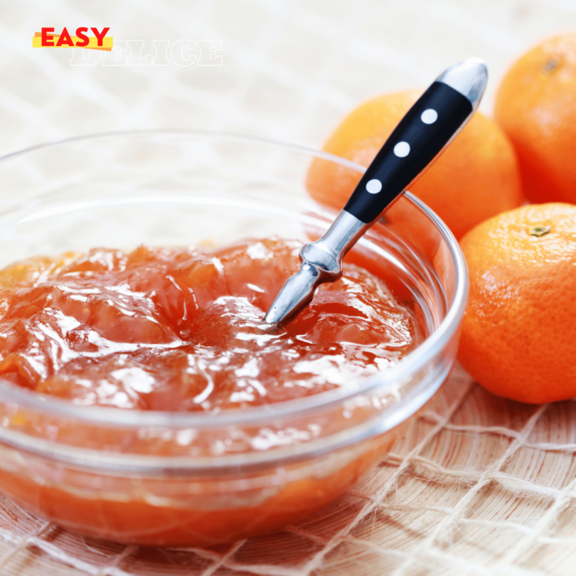 Pot de confiture de mandarines maison avec des tranches de mandarines fraîches et zestes.