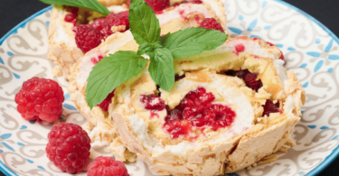 Une bûche au mascarpone, chocolat blanc et framboise élégamment décorée avec des framboises fraîches et des copeaux de chocolat blanc.