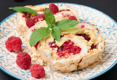 Une bûche au mascarpone, chocolat blanc et framboise élégamment décorée avec des framboises fraîches et des copeaux de chocolat blanc.