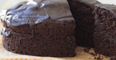 Un gâteau au chocolat sans sucre, moelleux et fondant, présenté avec une garniture de fruits rouges et une touche de cacao en poudre.