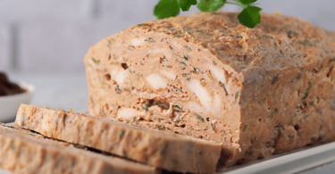 Terrine de poulet tranchée, garnie de légumes colorés et servie avec une salade verte.