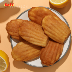 Madeleines dorées et moelleuses, légèrement bombées, parfumées au citron, servies sur une assiette élégante avec des zestes de citron.