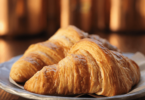 Croissants dorés et croustillants posés sur une grille de refroidissement, accompagnés d’un bol de café.